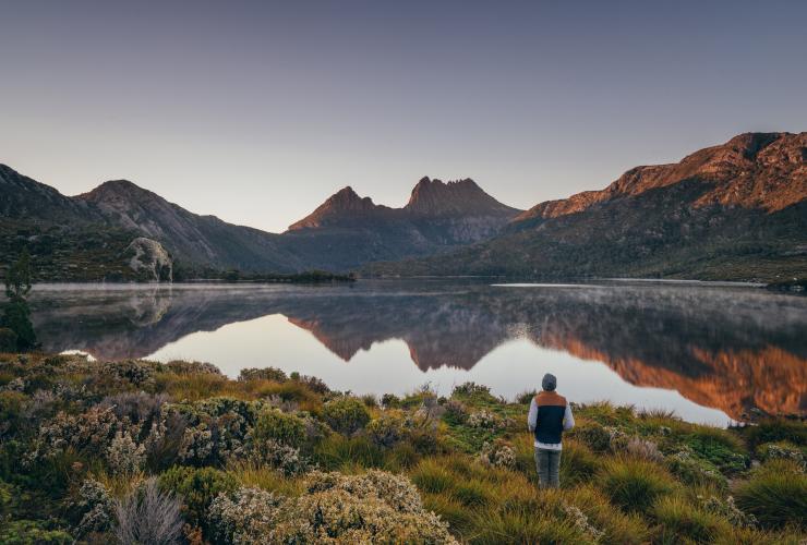 Una persona in piedi accanto alle acque cristalline di un lago circondato da montagne, The Overland Track, Cradle Mountain, Lake St Clair Cradle Mountain National park, Tasmania © Tourism Tasmania