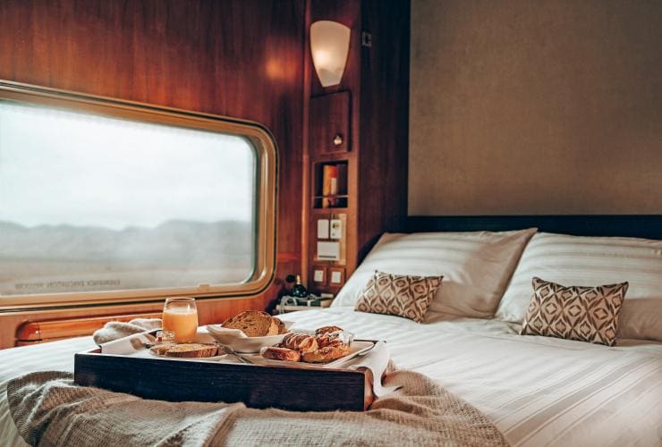 Colazione su un vassoio su un letto accanto al finestrino di un treno, The Ghan © Heather Dinas Photography