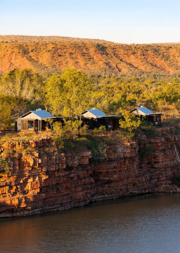 Accomodation presso El Questro Homestead circondate da alberi verdi sul margine di scogliere di roccia rossa a picco su un fiume a El Questro Wilderness Park, Western Australia © Timothy Burgess