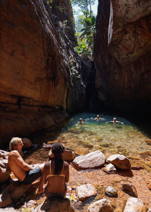 Gruppo di persone che nuotano in una caletta circondata da scogliere di roccia rossa a El Questro Wilderness Park, Kimberley, Western Australia © Tourism Australia