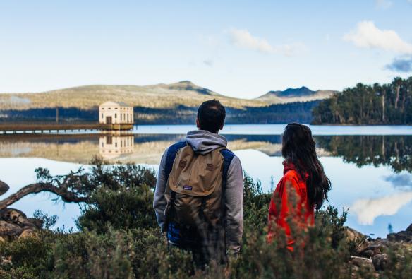 Coppia su un punto panoramico durante una camminata a Lake St Clair con Pumphouse Point in lontananza, Lake St Clair, Tasmania © Adam Gibson