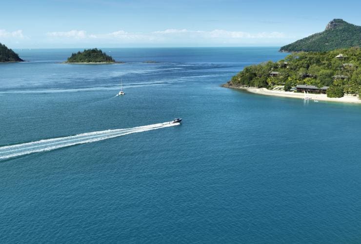 Barca che si avvicina alla spiaggia bianca circondata dal verde nei dintorni del qualia, Hamilton Island, Queensland © qualia