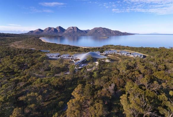 Vista aerea delle accomodation del Saffire Freycinet nascoste tra gli alberi, con Coles Bay e il Freycinet National Park sullo sfondo, Tasmania © Saffire Freycinet