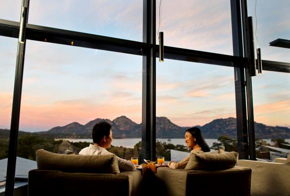 Coppia seduta su chaise longue con vista sulle montagne e sulle acque della Coles Bay al tramonto al Saffire Freycinet, Tasmania © Myka Photography