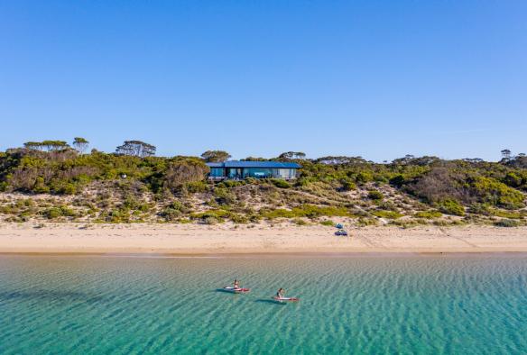 Due persone in kayak nell'oceano vicino a un alloggio sulla spiaggia, One Kangaroo Island, Kangaroo Island, South Australia © South Australian Tourism Commission