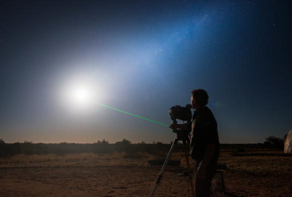 Uomo che punta un laser verso il cielo notturno pieno di stelle mentre guarda attraverso un telescopio all'Earth Sanctuary, Alice Springs, Northern Territory © Tourism NT/Matt Glastonbury