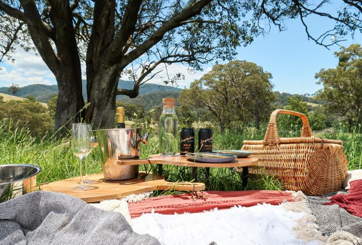Un picnic allestito su una collina erbosa sotto un albero, Picnic in the Paddock, Currajong Retreat, New South Wales © Amy Fraser