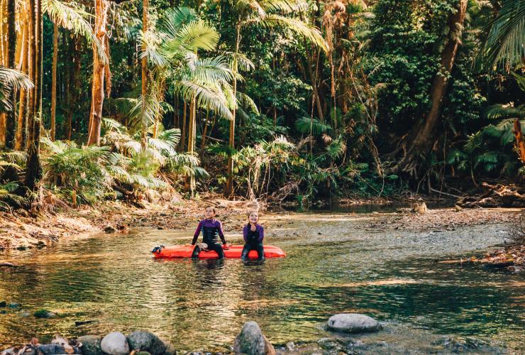 Due giovani che sorridono guardando gli alberi della foresta pluviale seduti su un materassino gonfiabile sul fiume durante un River Drift Snorkelling Tour, Back Country Bliss Adventures, Daintree, Queensland © Tourism Tropical North Queensland