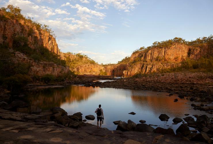 Escursionisti che fanno una sosta accanto a un lago immobile circondato da scogliere rosse nel Nitmiluk National Park, Northern Territory © Tourism NT/Matt Cherubino