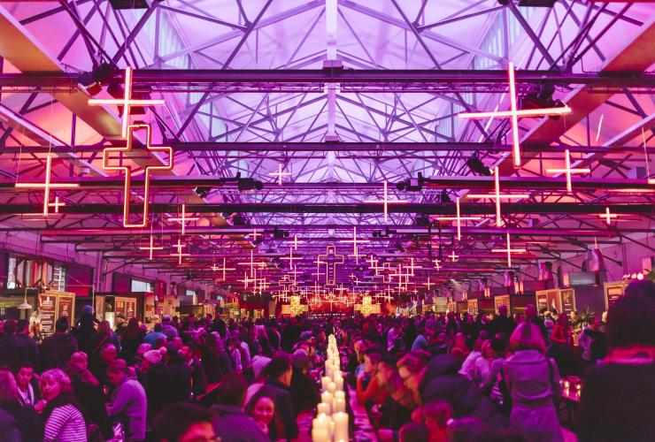 タスマニア州、ホバート、ダーク・モフォ・ウィンター・フィースト。紫とオレンジのライトの下、部屋いっぱいの人々が長いテーブルに着いている © Tourism Tasmania