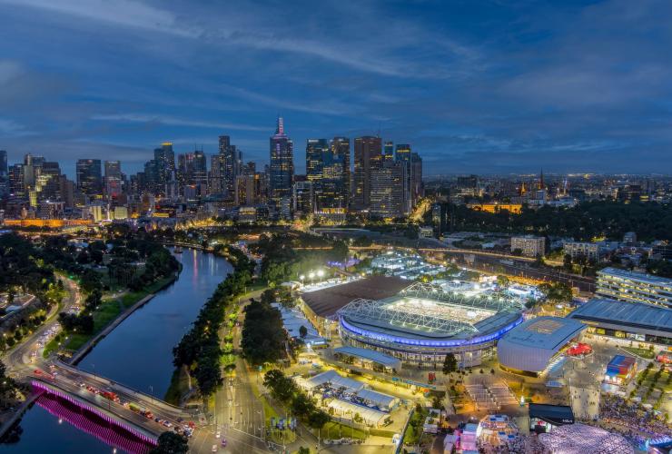 ビクトリア州、メルボルン、全豪オープンテニス。ライトアップされたスタジアムと街の夜景の空撮 © Nick La Galle