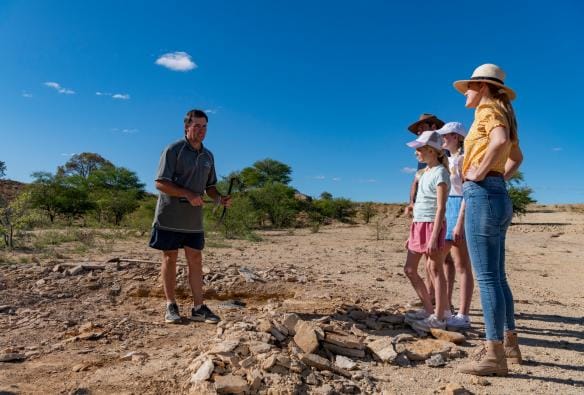 クイーンズランド州、リッチモンド、クロノサウルス・コーナーにて、土の中の化石を指し示すガイド © Tourism and Events Queensland