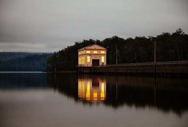 タスマニア州、夕暮れ時、セント・クレア湖の静かな水面に映るライトアップされたパンプハウス・ポイント宿泊施設と周囲の風景 © Tourism Tasmania