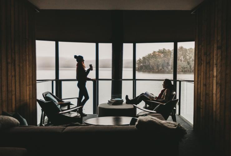 タスマニア州、パンプハウス・ポイントでセント・クレア湖の全景が見える窓のそばでくつろぐ男女 © Jarrad Seng