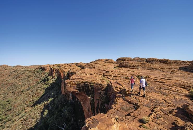 ノーザンテリトリー、キングス・キャニオン、リム・ウォーク沿いの崖の端近くをブッシュランドを下に見ながら歩く2人 © Tourism Northern Territory/Shaana McNaught