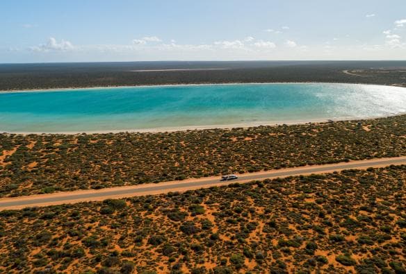 西オーストラリア州、デナム、シャーク湾、青い水と道路を走る車の空撮 © Tourism Australia 