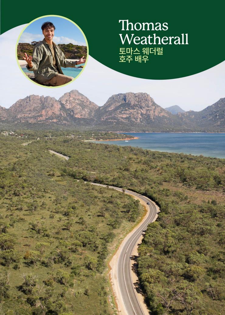 멀리 산과 넓은 수역이 보이는 숲속 도로를 항공으로 촬영한 사진, 그 위에 겹쳐진 웃고 있는 남자의 사진과 '호주 배우 토마스 웨더럴'이라는 문구