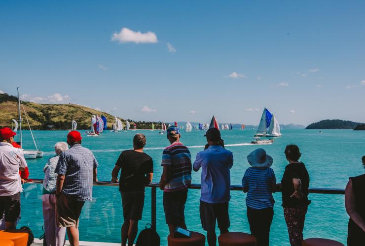 Một nhóm người đứng trên bờ ngắm nhìn những cánh buồm nhiều màu sắc trong Tuần lễ đua thuyền Đảo Hamilton, Đảo Hamilton, Queensland © Tourism Australia