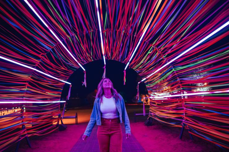 Một người đứng dưới vòm ánh sáng rực rỡ sắc màu tại Lễ hội Parrtjima, Thị trấn Alice Springs, Lãnh thổ phía Bắc © Tourism NT