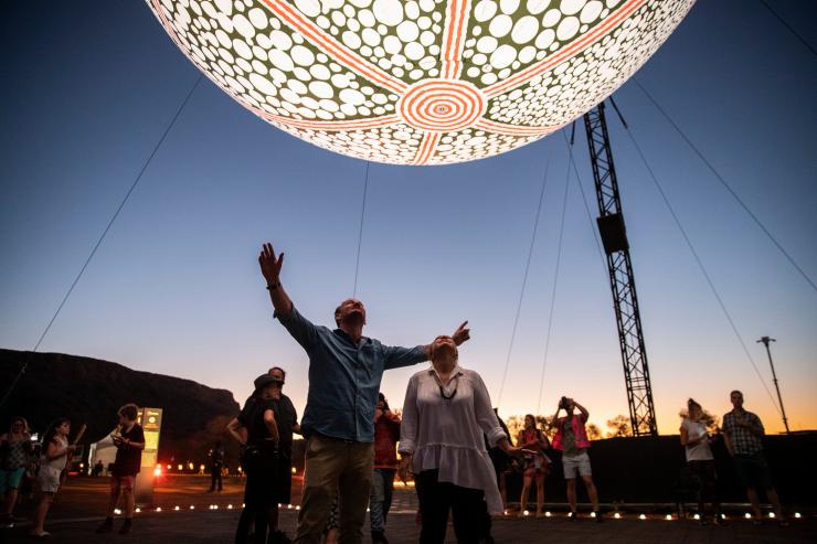 Một cặp đôi đứng dưới một tác phẩm ánh sáng hình tròn phát sáng tại Lễ hội Parrtjima, Thị trấn Alice Springs, Lãnh thổ phía Bắc © Tourism NT