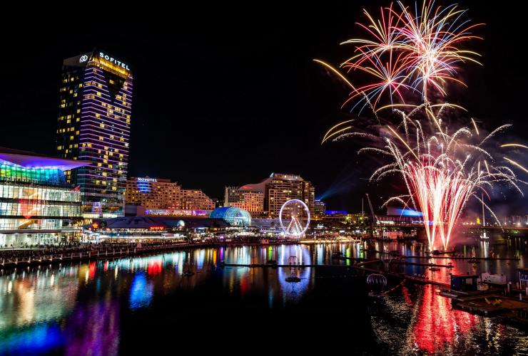 Một khu bến cảng được bao quanh bởi các toà nhà phủ ánh đèn nhiều màu khi pháo hoa bắn lên trong sự kiện Vivid Sydney, Sydney, New South Wales © Destination NSW