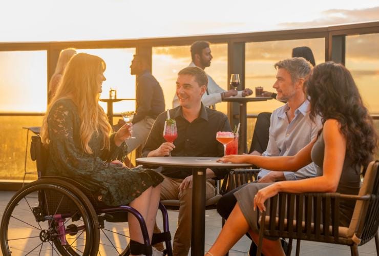 Một nhóm bạn, trong đó có một người sử dụng xe lăn, cùng thưởng thức đồ uống tại Sol Rooftop, thành phố Adelaide, tiểu bang Nam Úc © Tourism Australia
