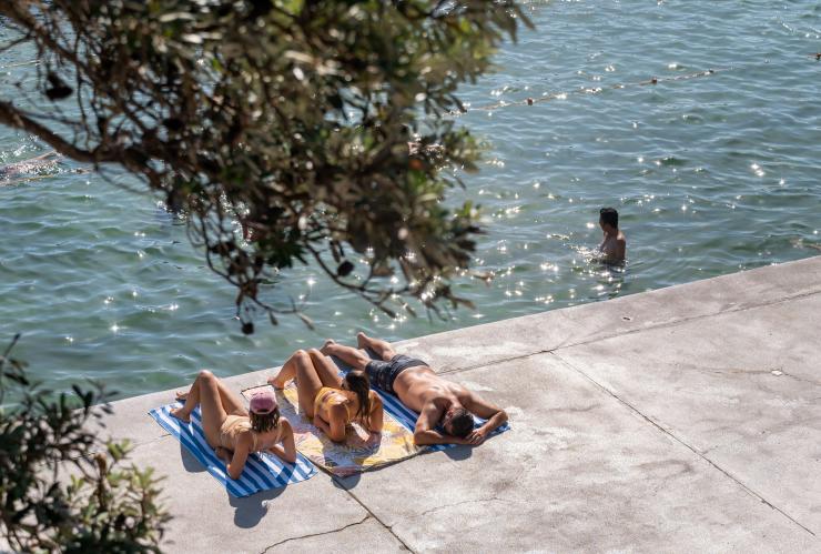 Ba người bạn nằm trên khăn tắm bên mép nước tại thị trấn The Entrance, Bờ biển Central Coast, tiểu bang New South Wales © Tourism Australia