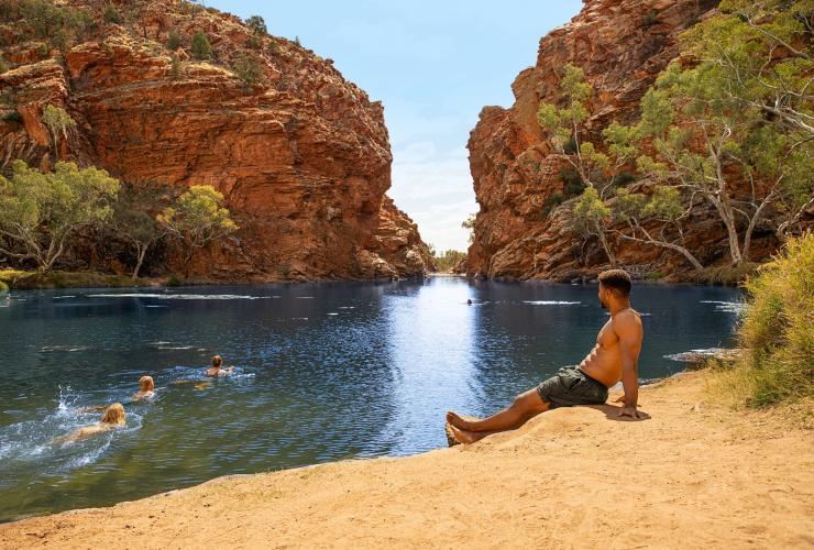 Một người đàn ông ngồi trên cát gần hồ Ellery Creek Big Hole, Dãy núi West MacDonnell, Lãnh thổ phía Bắc © Tourism Australia