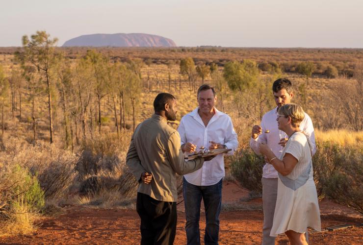 Một nhóm người được phục vụ các món khai vị trong khung cảnh nhìn ra Uluru, với trải nghiệm ẩm thực Tali Wiru, Uluru, Lãnh thổ phía Bắc © Tourism NT/Tourism Australia