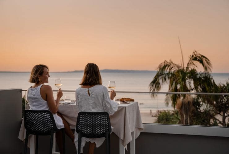 Hai người phụ nữ hướng nhìn ra đại dương trong khi thưởng thức rượu vang tại thị trấn Noosa Heads, Vùng Sunshine Coast, tiểu bang Queensland © Tourism Australia