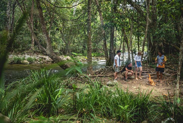 A group of people standing around a campfire in a rainforest beside a river with Walkabout Cultural Adventures, Port Douglas, Tropical North Queensland, Queensland © Tourism and Events Queensland 