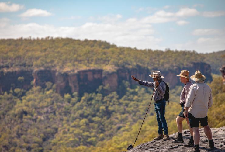 Two people standing with a tour guide on a rocky ledge overlooking bushland during a tour with Jarramali Rock Art Tours, Cape York, Queensland © Tourism and Events Queensland