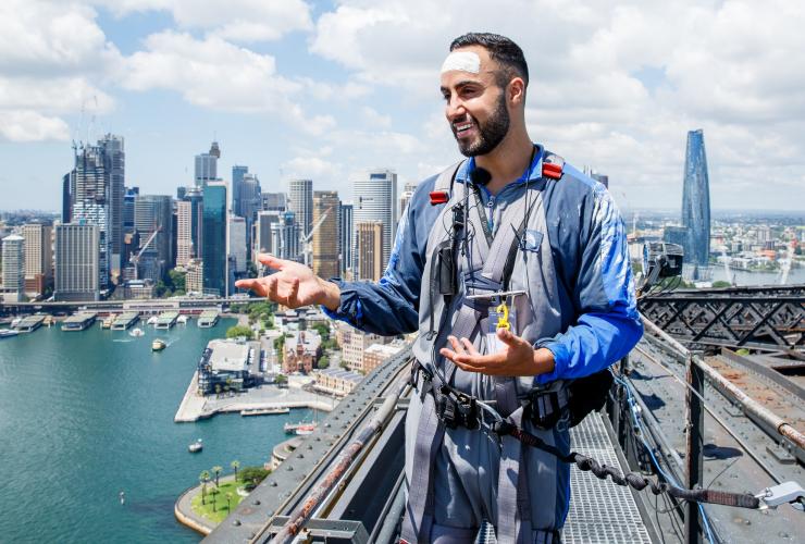 An Aboriginal guide wearing white paint on their forehead while standing on top of a bridge overlooking a harbour city during the Burrawa Climb, Sydney Harbour Bridge, Sydney, New South Wales © Feliz Puente