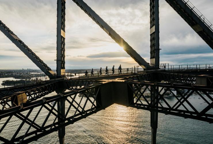 A group of people climbing a steel arch bridge over a harbour during the Burrawa Climb on the Sydney Harbour Bridge, Sydney, New South Wales © Destination NSW 