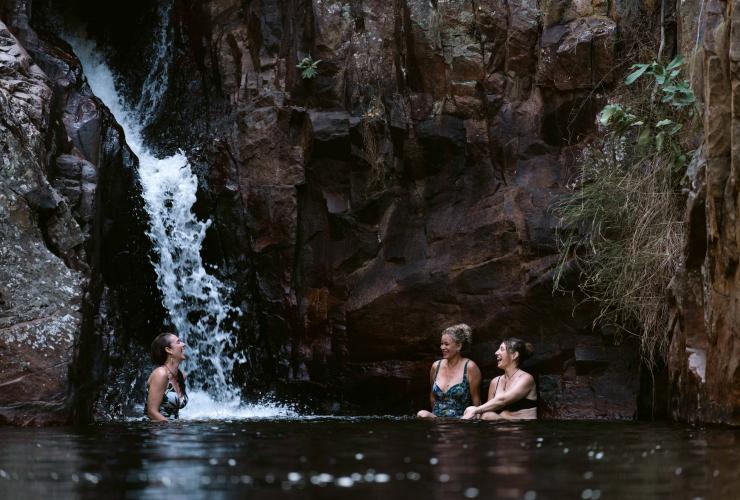 Three people swimming beneath a small waterfall during a tour with Lords Kakadu & Arnhem Land Safaris, Kakadu National Park Northern Territory © Tourism Australia 