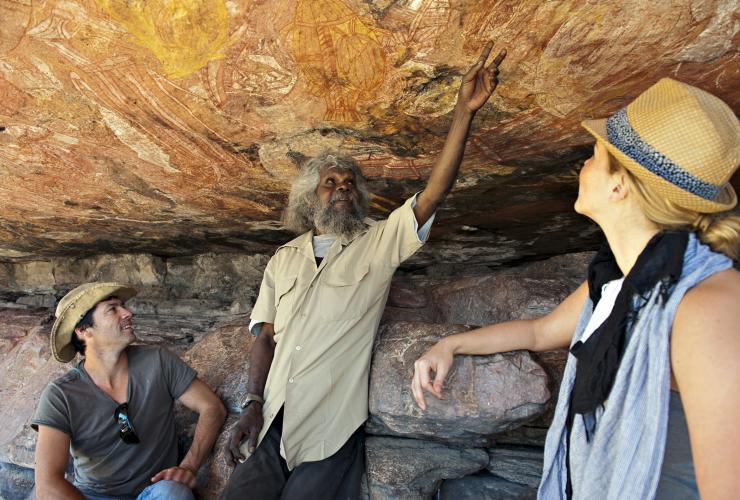 An Aboriginal guide describing ancient rock art to guests standing beneath a rocky outcrop with Lords Kakadu & Arnhem Land Safaris, Injalak Hill, Northern Territory © Shaana McNaught 