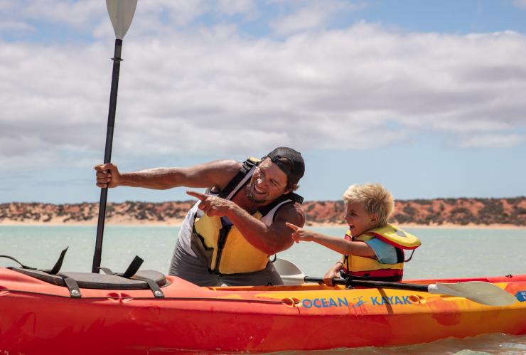 An Aboriginal tour guide standing in the water beside a kayak smiling and pointing with a child during a tour with Wula Gura Nyinda Eco Cultural Adventures, Coral Coast, Western Australia © James Fisher/Tourism Australia