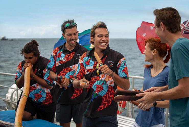 Aboriginal tour guides performing using clapping sticks and didgeridoos on a boat during a tour with Dreamtime Drive and Snorkel, Great Barrier Reef. Cairns, Queensland © Archie Sartracom