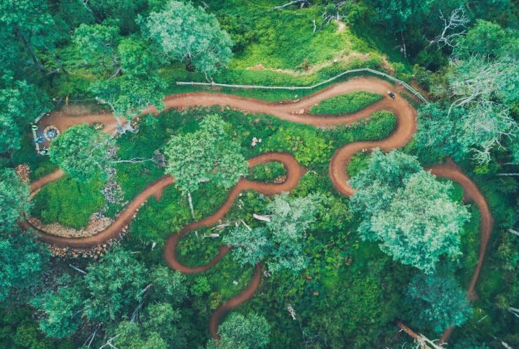 Aerial view over a green grassy area with a mountain bike track carved in loops amid bushland at Blue Derby Mountain Bike Trails, Derby, Tasmania © Flow Mountain Bike