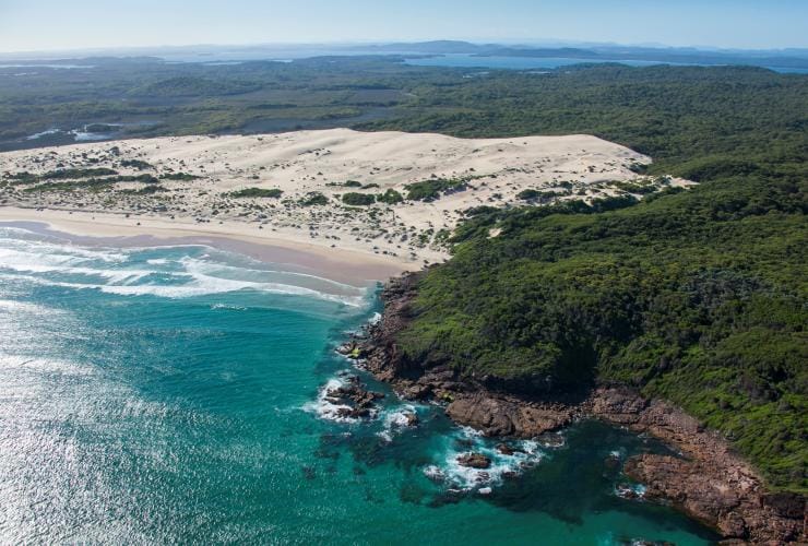 Aerial view over a white sand beach with turquoise water and green bushland at Samurai Beach, Port Stephens, New South Wales © Destination NSW