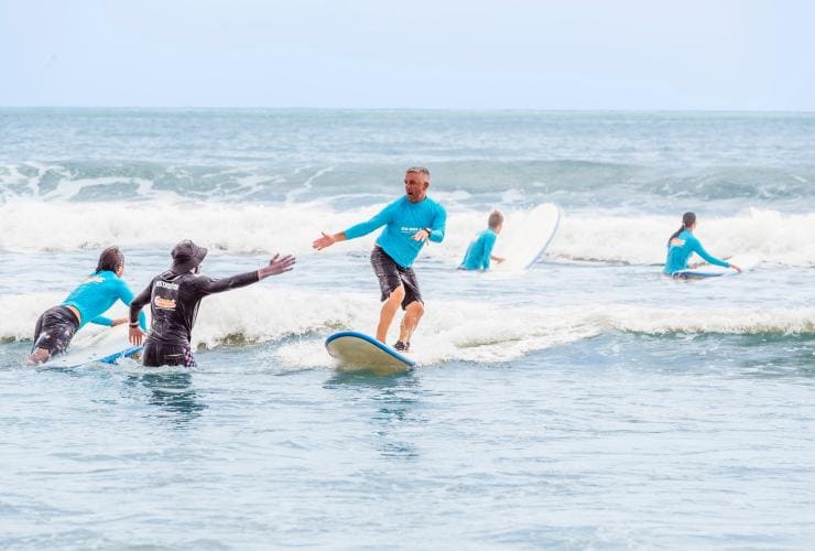 An instructor stands waist-deep in the ocean and gives a surfer a fist-bump in Noosa, Queensland © Tourism and Events Queensland