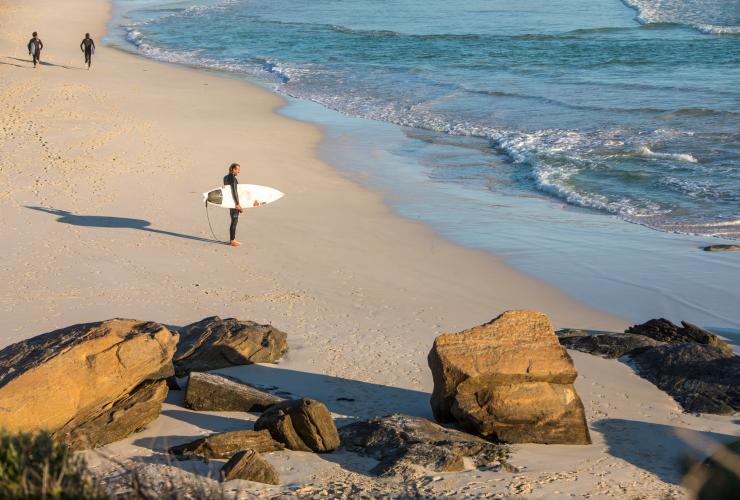 A surfer stands with a surfboard beneath his arm, looking toward the ocean at Redgate Beach in Margaret River, Western Australia © Martine Perret