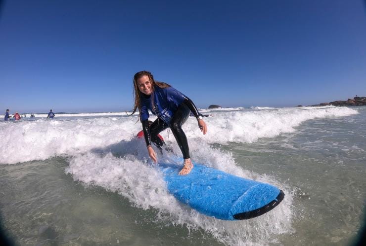 A woman crouches on a surfboard as a wave brings her toward shore at Redgate Beach in Margaret River, Western Australia © Tourism Australia