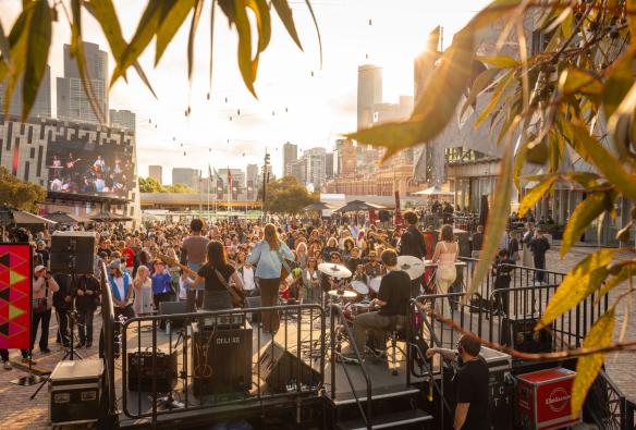 A crowd watches a live music gig with the Melbourne skyline in the background at Federation Square, Melbourne, Victoria © Always Live