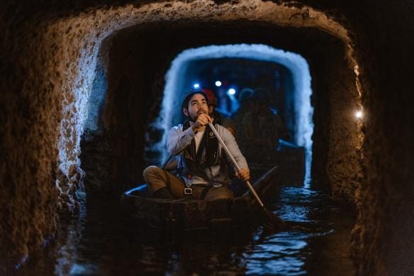 A man wearing a head lamp paddles in a small boat amongst old tunnels on the Fremantle Prison Tunnels Tour, Fremantle, Western Australia