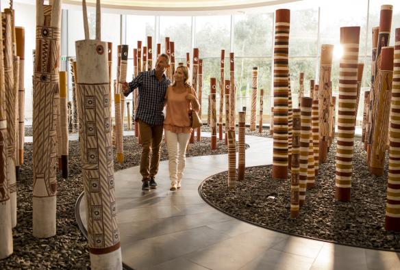 A couple walks through a collection of poles painted with Indigenous art at the Aboriginal Memorial, National Gallery of Australia, Canberra, Australian Capital Territory © Tourism Australia