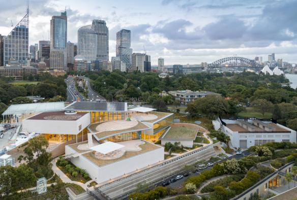 Aerial view over a tiered building with outdoor sculptures surrounded by green trees with a city skyline behind it at the Art Gallery of New South Wales, Sydney, New South Wales © Art Gallery of New South Wales / Tourism Australia