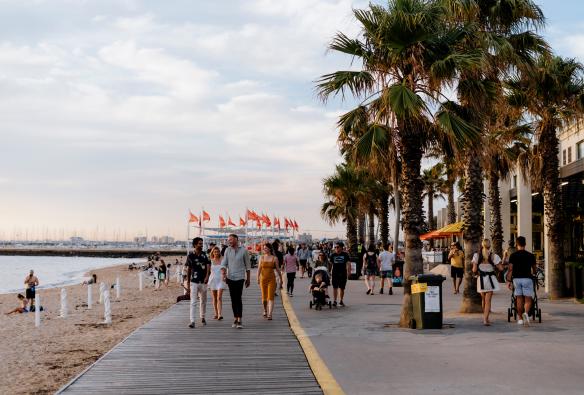 Groups of people walking along the palm tree-lined boardwalk of St Kilda beach in Melbourne, Victoria © Visit Victoria