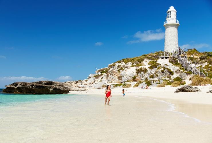 Trẻ em nô đùa trong làn nước êm đềm trên bãi biển cát trắng, cạnh ngọn hải đăng trên một mũi đất, Bãi biển Pinky, Đảo Rottnest, Tiểu bang Tây Úc © Rottnest Island Authority