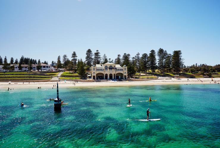 Góc nhìn từ phía biển hướng vào bãi biển cát trắng, với những người chèo ván đứng trên làn nước xanh ngọc trong vắt, tại Bãi biển Cottesloe, Thành phố Perth, Tiểu bang Tây Úc © Tourism Western Australia